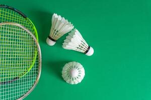 Two badminton rackets with shuttlecocks placed on a green background, offering ample copy space. photo