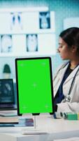 Vertical Female general practitioner and patient looking at green screen on tablet, recommending pills and drugs during check up. Indian people discussing about diagnostic report and remedy. Camera B. video