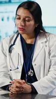 vertical especialista y paciente que se discute diagnóstico resultados en un moderno médico oficina, estableciendo avanzado cuidado de la salud tecnología a presente X rayo imagen resultados y mri escaneos cuidado gestión. cámara una. video