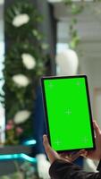 Vertical Asian retail assistant holding a tablet with green screen in clothing store, creating a tidy chic display that enhances the shopping experience for clients. Employee works at a mall. video