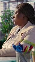 Vertical Black business director resting in her high end CEO chair after a project, reminiscing about her career development and achievements. Female leader taking a break to relax at work. Camera B. video