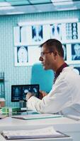 Vertical General practitioner consulting patient and reviewing x ray test results, utilizing technology for an analysis and patient care management in a medical environment. Healthcare provider. Camera B. video