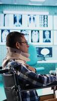 Vertical Indian patient with impairment and cervical foam attends a check up with specialist, discussing about treatment and a recovery plan. Sick wheelchair user listens to scan interpretation. Camera B. video