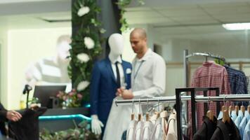 Designer boutique assistant arranging a vibrant selection of garments on racks, highlighting stylish new collection apparel and creating a welcoming shopping experience for customers. Camera A. video