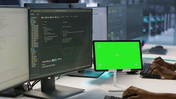 IT experts using green screen tablet, working together in server farm to optimize it for data processing requirements. Close up of coworkers coding on chroma key device in data center, camera A video