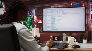Programmer at computer desk coding, creating software, implementing algorithms. African american IT specialist in home office working with code editor, building applications, camera A video