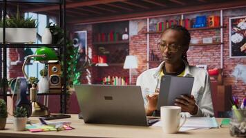 Woman at home taking break from work to look at social media feed on tablet. Remote employee at work in apartment office pausing tasks to use social network application on device, camera A video