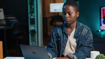 Freelancer in neon lit home office sitting at desk and typing on laptop keyboard. Remote employee using electronic device to do customers relations job online, answering inquiries, camera A video