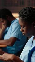 Vertical African american medical assistant prepares for exams in a library, reading medical methods and reviewing anatomy lessons from old case files and research papers. Healthcare education. Camera B. video