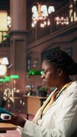Vertical Black woman student in med school using an oximeter and reading about the practice, studying with academic database copy books at the library. Scholar does her medical research. Camera A. video