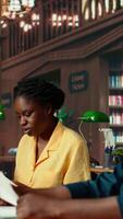Vertical African american students learning a foreign language together at the university library, consulting books from the academic database. Class colleagues helping each other study for exams. Camera B. video