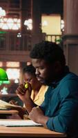 Vertical African american pupil underlining key words and phrases at the library, creating a summary with the highlighter pen at a university campus study space. Academic research for exams. Camera A. video