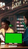Vertical African american students consulting research papers next to green screen from the academic database, learning information from copy books. Young team of pupils at the library. Camera A. video