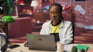 Student at home drinking coffee and browsing internet on notebook, researching information online. Woman enjoying hot beverage while reading internet articles on laptop for school tasks, camera B video