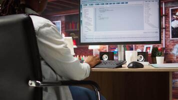 Programmer wearing headphones types code into PC, developing software programs, entering commands. Woman at home fixing errors in application, implementing new features, listening music, camera A video