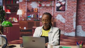 Remote worker at home office desk drinking coffee and browsing internet on notebook, researching information. Woman enjoying hot beverage while using search engines to find data for work, camera B video