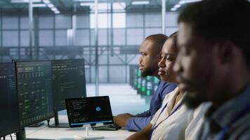 Focus on server hub employee developing disaster recovery plans ensuring minimal downtime. African american man in data center using data analytics to monitor performance, camera A video