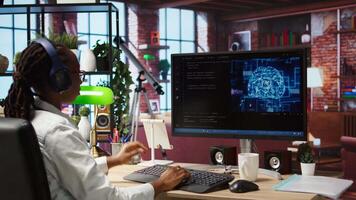 Software developer wearing headphones using computer at home for artificial intelligence computing simulating human brain. IT expert listening music and working with AI deep neural networks, camera A video