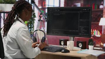 Developer at computer desk coding while listening music, creating software, implementing algorithms. Remote worker with headphones on at home working with code editor, building applications, camera B video