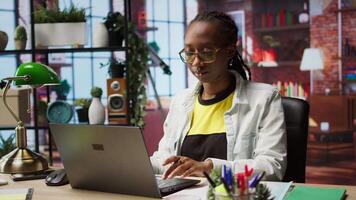 Teleworker analyzing data on laptop at desk and looking over paperwork, compiling analytical reports. Remote employee checking documents, using notebook to upload company information online, camera A video
