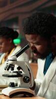 verticale Masculin étudiant recherche virus pendant une microscope une analyse et académique en train de lire dans une classique bibliothèque. med école élève reflète dévouement à la biologie et examen les préparatifs. caméra b. video