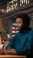 Vertical Students team read through an academic project in a classic library, showcasing their commitment to education and self improvement. Black pupils work together on their academic growth. Camera A. video