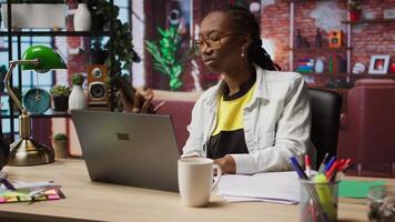 Woman in home office sitting at desk in front of laptop, answering phone call. Remote employee using notebook to do job online, receiving telephone call on smartphone, camera A video
