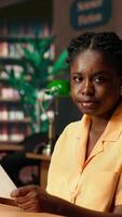 Vertical Dedicated black student reviewing papers in a traditional library setting, focusing on educational goals and study time within the campus. College girl studies and does research. Camera B. video