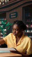 Vertical African american pupil highlighting key words from the class notes, creating a summary to study easily and memorize the lesson theory. Student using a learning technique in the library. Camera A. video