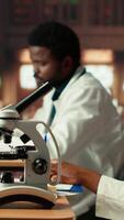 vertical hembra Universidad estudiante se enfoca en médico Ciencias por utilizando un microscopio, examinando el químico procesos de microorganismos mujer estudiando para su académico tesis papel. cámara b. video