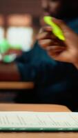 Vertical African american scholar highlighting the relevant information from class notes, creating a summary with highlighter pen. Student underlining key words and phrases from the course. Camera B. video