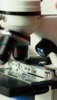 verticale futur chercheur travaux sur sa thèse par examiner microorganismes en dessous de le microscope lentilles, en train de lire à propos microbiologie et médical science. concentrer sur scientifique examens. proche en haut. caméra b. video