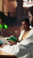 Vertical Black medical students comparing knowledge and class notes at the library, studying together to obtain their residency. Pupils learning healthcare methods by reading surgery notes. Camera A. video