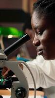verticale futur chercheur travaux sur sa thèse par examiner microorganismes en dessous de le microscope lentilles, en train de lire à propos microbiologie et médical science. concentrer sur scientifique examens. proche en haut. caméra un. video