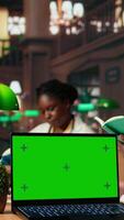 Vertical African American med student reading a healthcare book next to copy space, focusing on medical practice methods under green lamps in a classic library. Commitment to education. Camera A. video