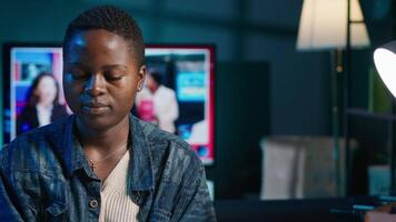 Portrait of smiling african american woman at desk typing on laptop keyboard, solving tasks. Joyful remote worker using notebook to send emails to business partners from living room, camera A video