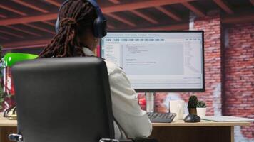 Programmer wearing headphones types code into PC, developing software programs, entering commands. Woman at home fixing errors in application, implementing new features, listening music, camera B video