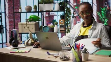 Remote worker at home office desk looking over folder files and using laptop, drafting contracts. Remote employee checking paperwork documents in front of notebook, camera A video