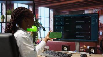 Woman using green screen smartphone to learn how to use AI LLM chatbot on computer screen in home office. Person watches tutorial on mockup phone about artificial intelligence chatbots, camera A video