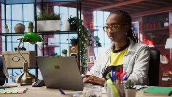 Freelancer at home checking analytics statistical data sets on laptop, comparing with paperwork files. Woman optimizing key performance indicators on notebook by crosschecking with documents, camera A video