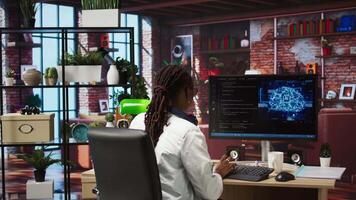 Admin uses computer for artificial intelligence computing simulation, waiting for code to finish compiling. African american woman works with AI deep neural networks at home, camera A video