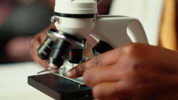 African american scholar studies medical science in a college library, doing research on viruses using a microscope. Girl works on exam preparation for success in a scientific career. Camera B. video