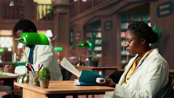 Black woman student in med school using an oximeter and reading about the practice, studying with academic database copy books at the library. Scholar does her medical research. Camera B. video