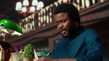 Black university student feeling anxious and struggling with learning, trying to memorize relevant information from course notes at the library. Male pupil studying to pass exams. Camera B. video