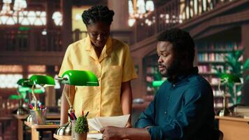 Students team read through an academic project in a classic library, showcasing their commitment to education and self improvement. Black pupils work together on their academic growth. Camera B. video