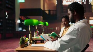 Black medical students comparing knowledge and class notes at the library, studying together to obtain their residency. Pupils learning healthcare methods by reading surgery notes. Camera A. video