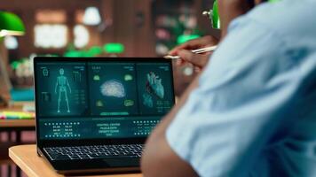 Med school student takes personal notes from anatomy research papers, studying healthcare methods for a medical career. Male scholar using books from the campus databases. Camera B. video
