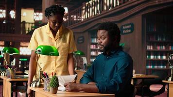Students team read through an academic project in a classic library, showcasing their commitment to education and self improvement. Black pupils work together on their academic growth. Camera A. video