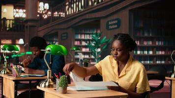 African american pupil highlighting key words from the class notes, creating a summary to study easily and memorize the lesson theory. Student using a learning technique in the library. Camera A. video