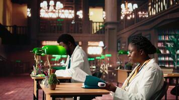 Black woman student in med school using an oximeter and reading about the practice, studying with academic database copy books at the library. Scholar does her medical research. Camera A. video